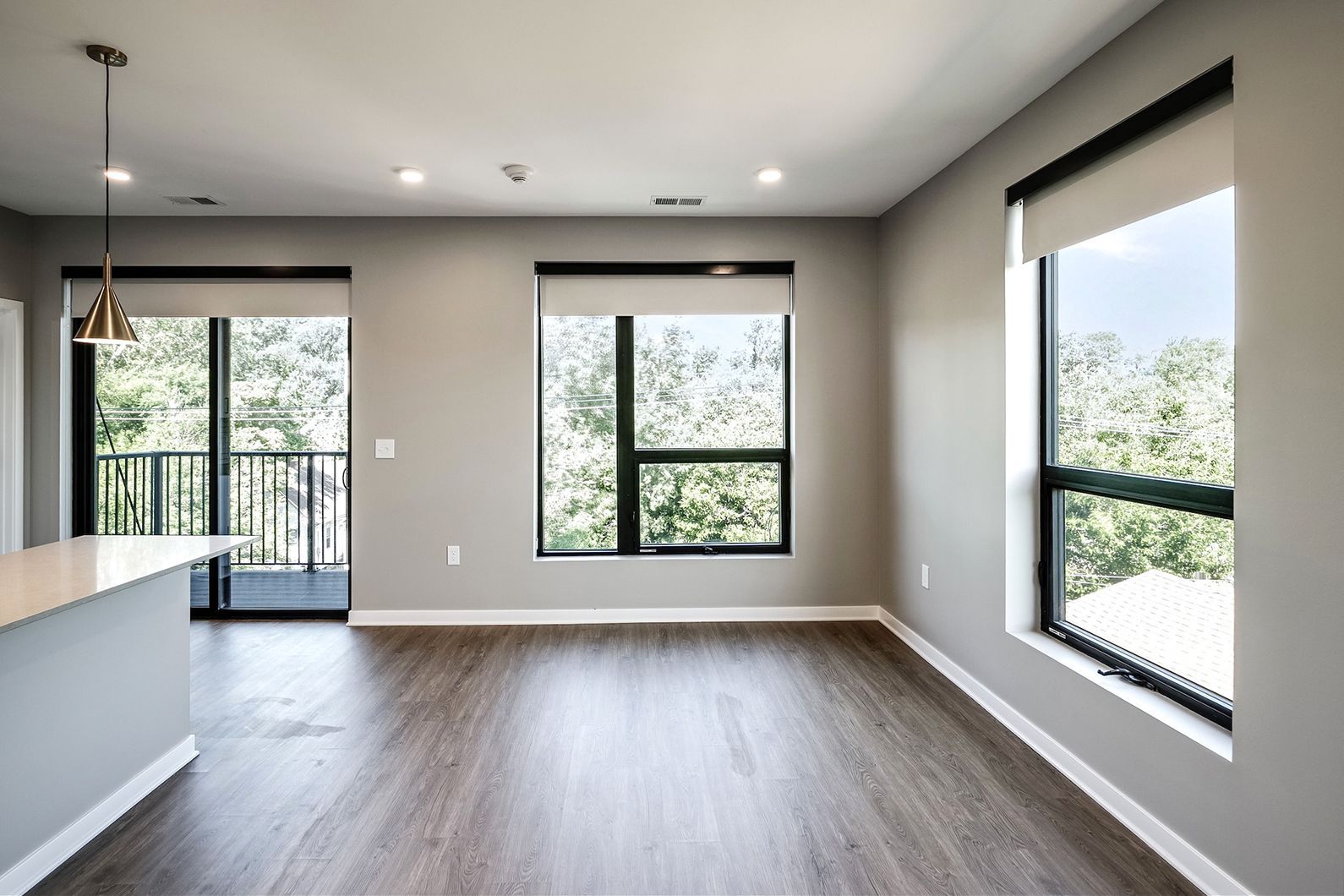 Empty modern living room with gray walls, wood floors, and large windows overlooking greenery