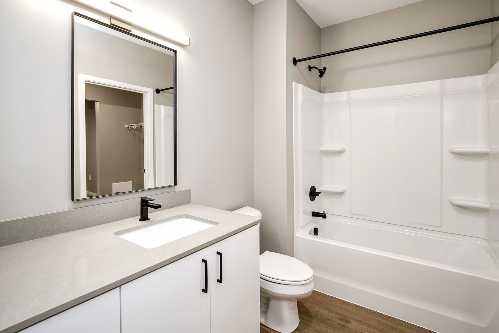 Modern bathroom with white vanity, black fixtures, mirror, toilet, and tub with shower curtain