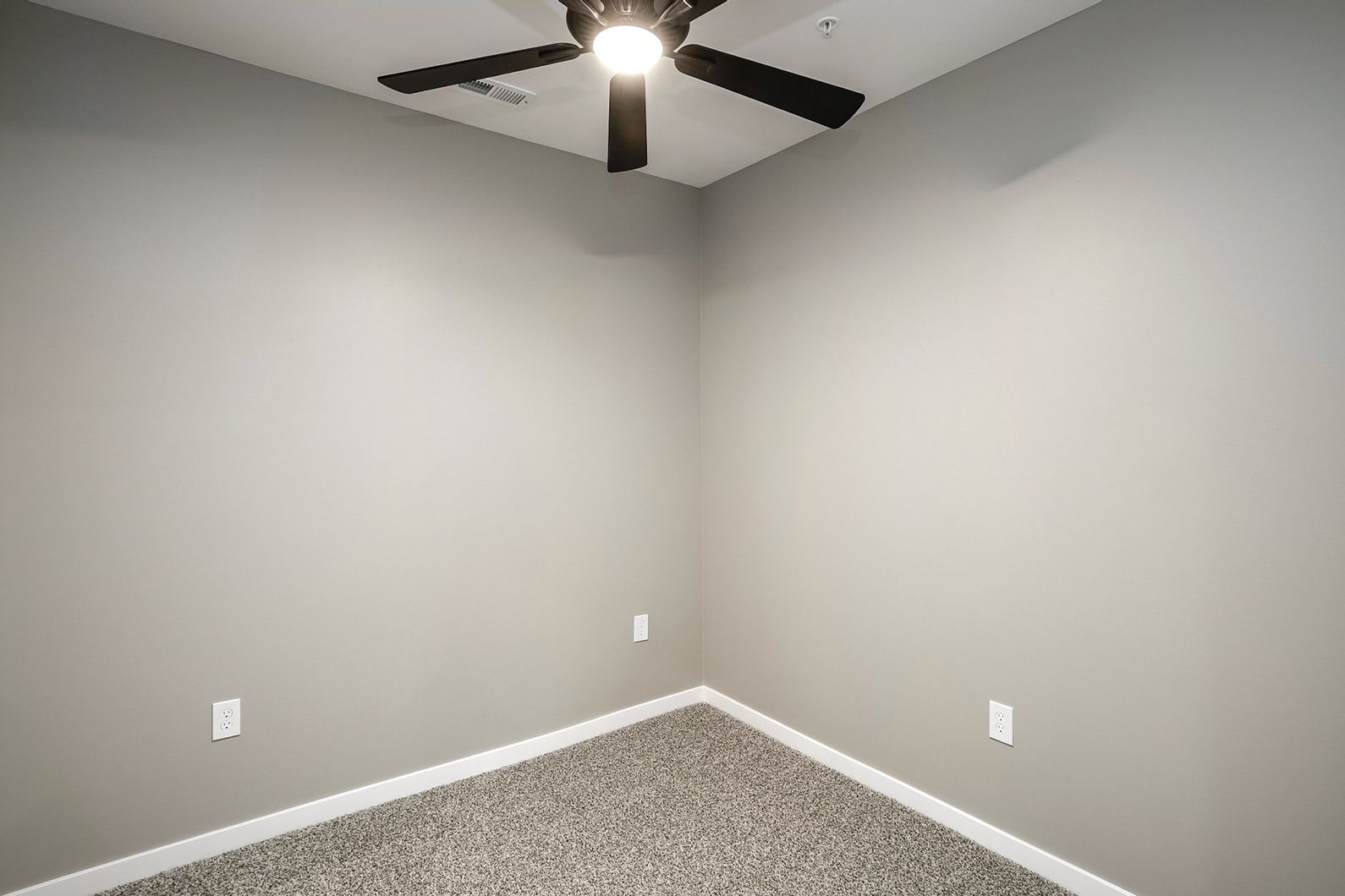 Empty gray bedroom corner with carpet and ceiling fan light