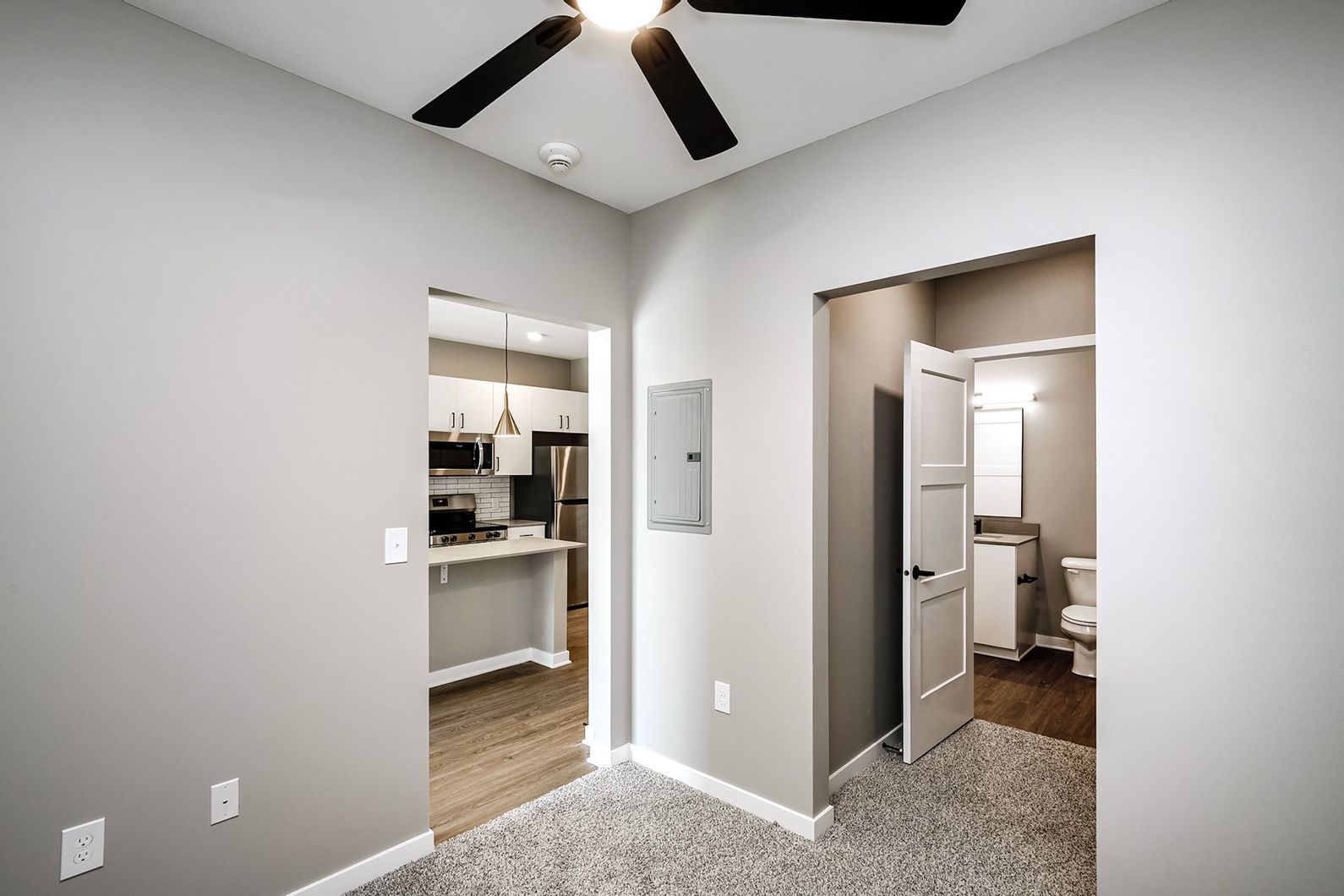 Empty bedroom with gray walls, ceiling fan, and two open doorways to closet and bathroom