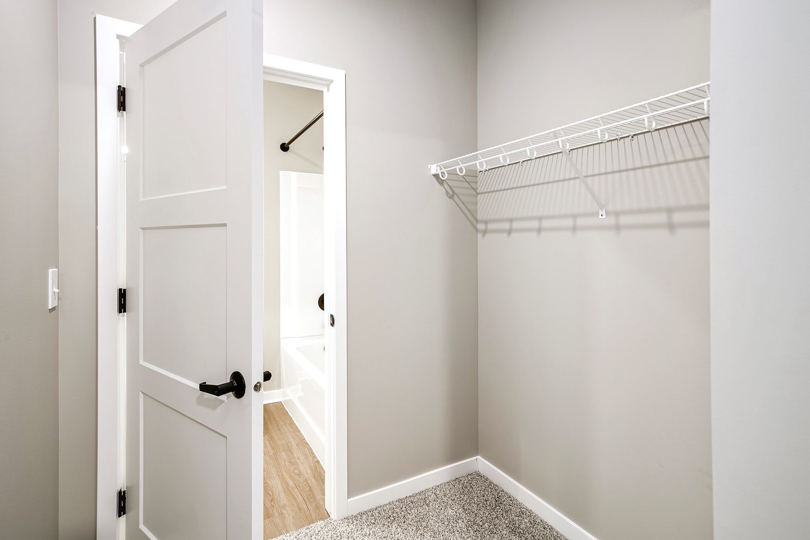 Empty walk-in closet with white wire shelving, open door, and light gray walls.