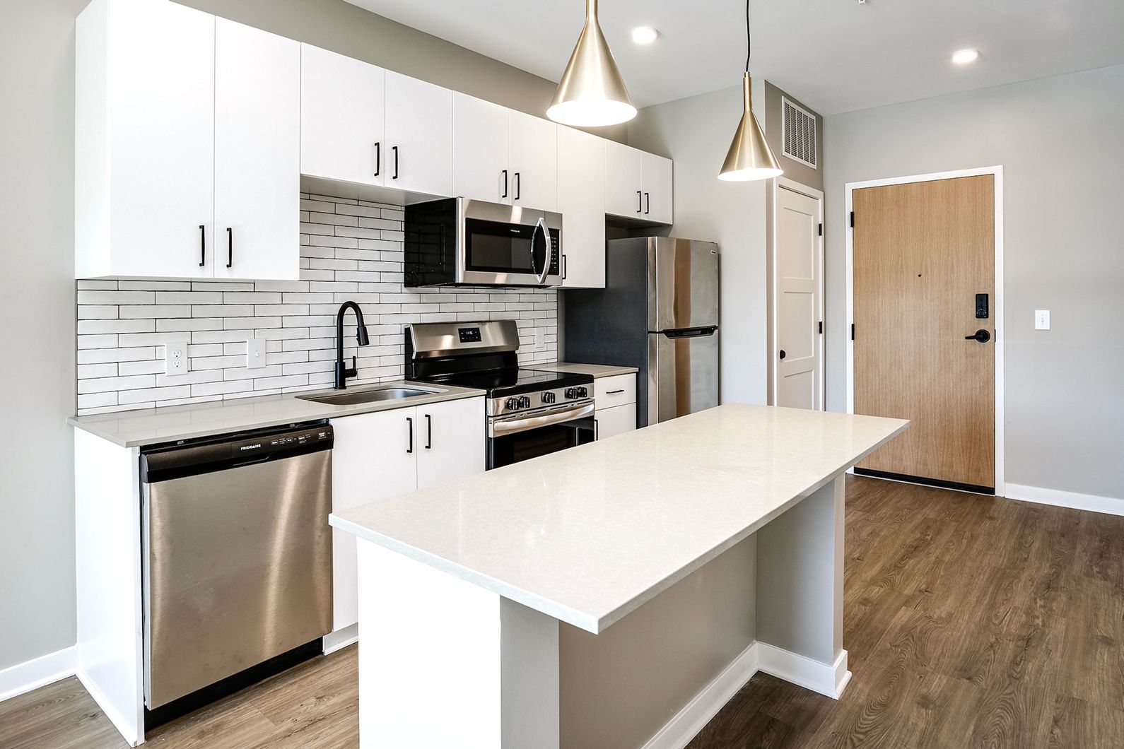 Modern kitchen with white cabinets, island, stainless steel appliances, pendant lights, and wood flooring