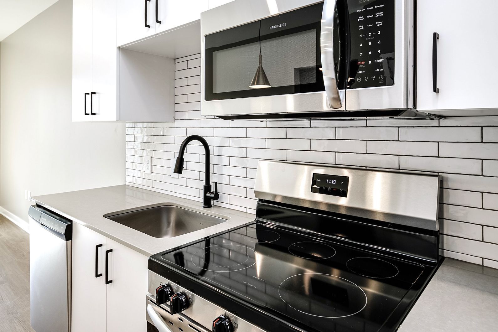 Modern white kitchen with black appliances, subway tile backsplash, and stainless steel sink and stove