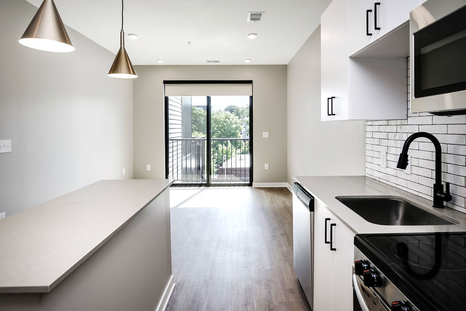Modern white kitchen with black accents, pendant lights, island, and sliding glass doors to a balcony