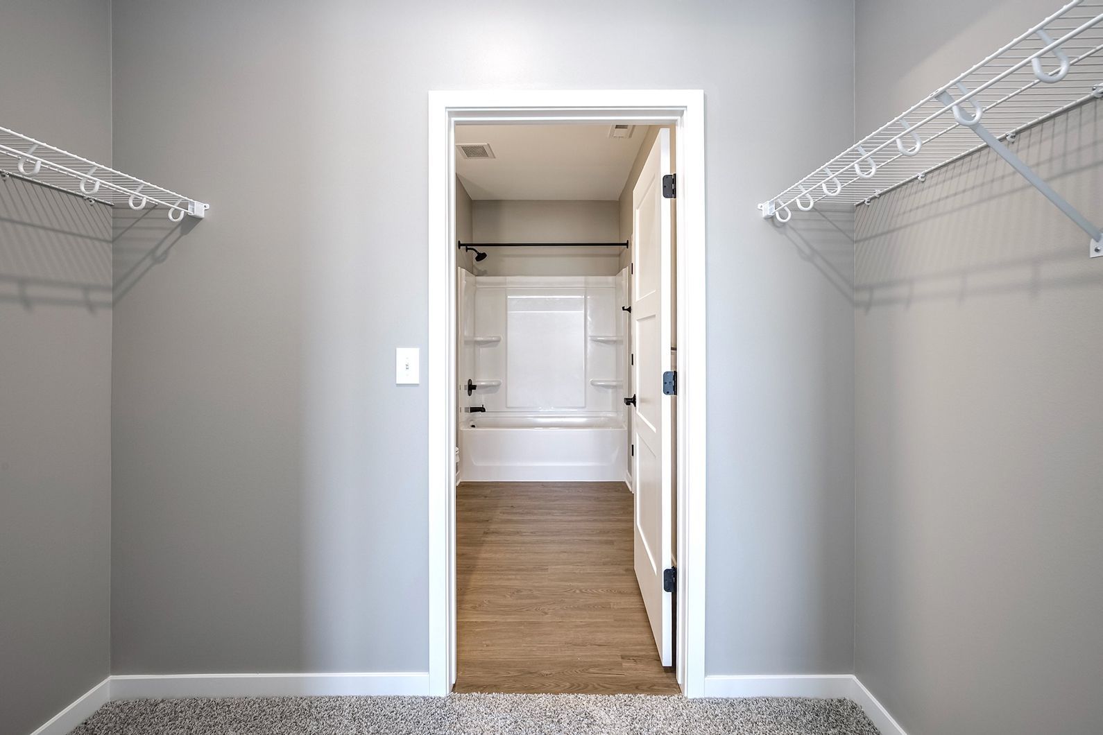 Empty walk-in closet with white wire shelving, gray walls, and a doorway to a carpeted room.