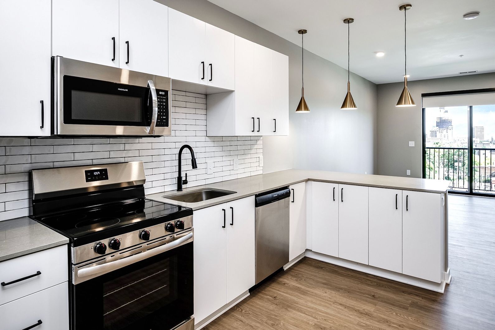 Modern white kitchen with black appliances, gray backsplash, wood floor, and large window