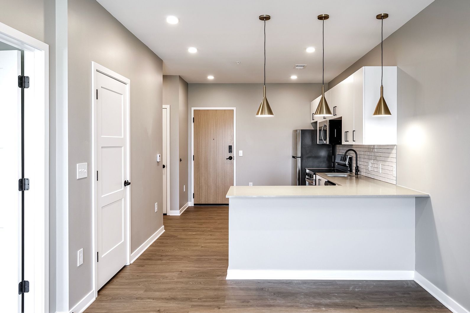 Empty modern kitchen with white cabinets, pendant lights, and dark wood floors