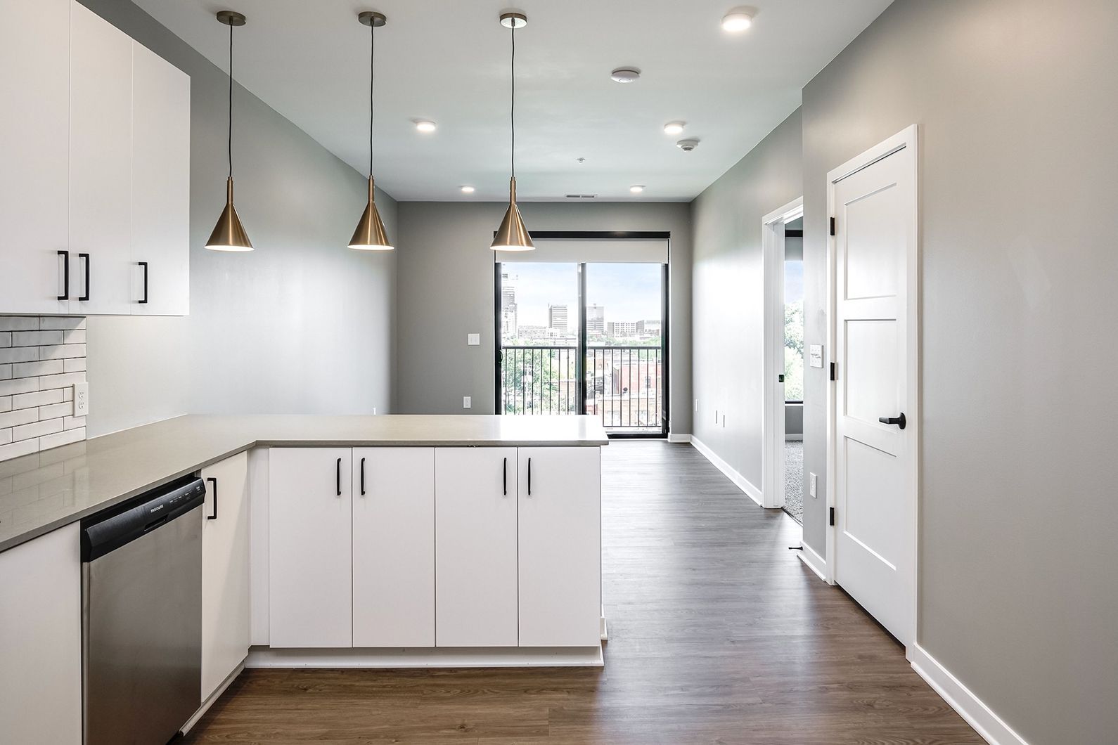 Modern empty kitchen with white cabinets, pendant lights, gray walls, and a sliding glass door.