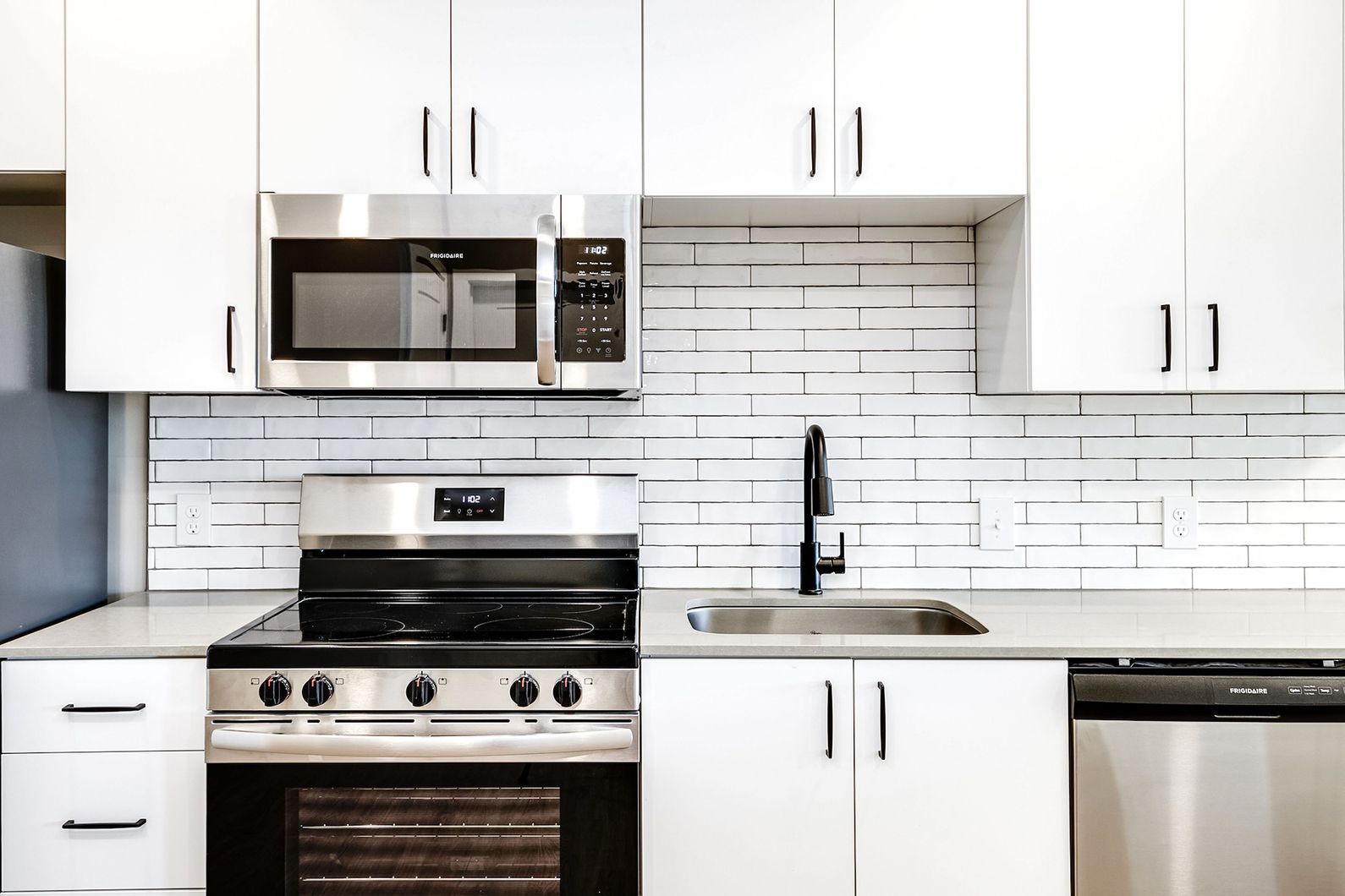 Modern white kitchen with stainless steel appliances, black countertops, and subway tile backsplash