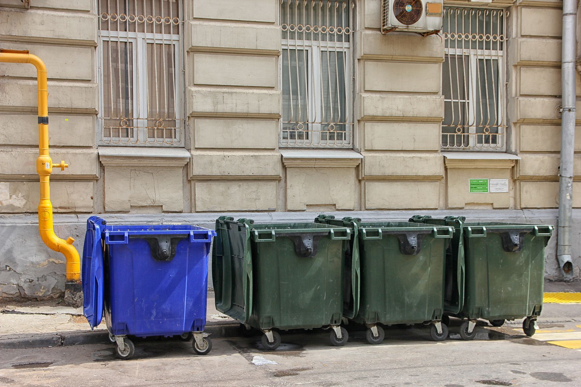 one blue and three green dumpsters outside a stone building
