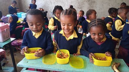 Children seated at a table eating from yellow bowls in a classroom
