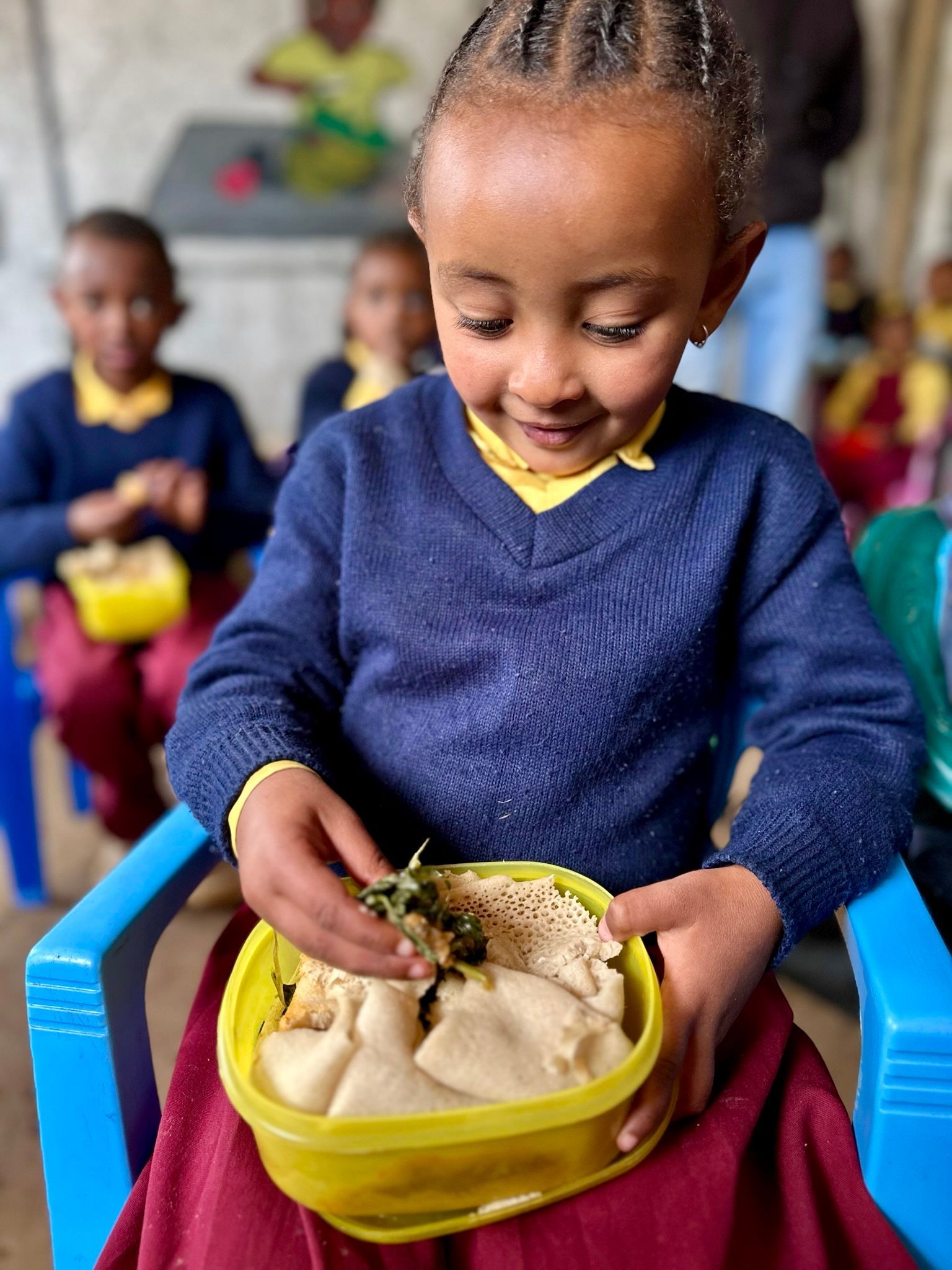 Children smiling and eating flatbread with bean dishes in a classroom