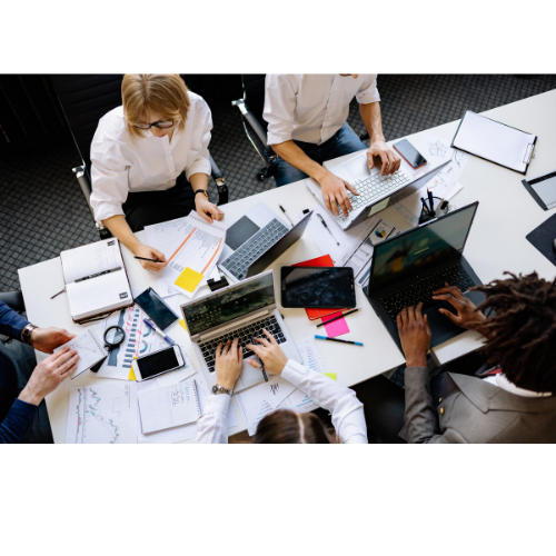 People working collaboratively at a white table with laptops, papers, and mobile devices regarding salary benchmarking.