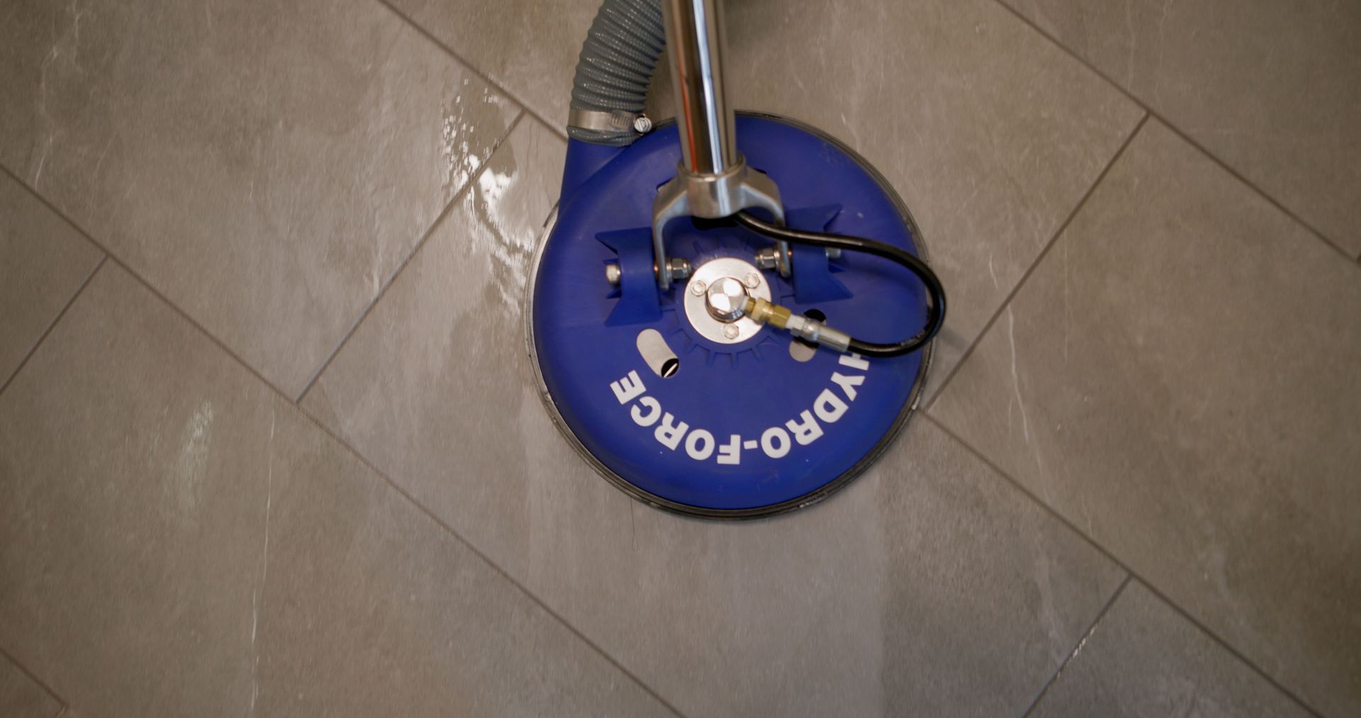 A blue Hydro-Force floor cleaning tool on a gray tiled floor, cleaning with water.