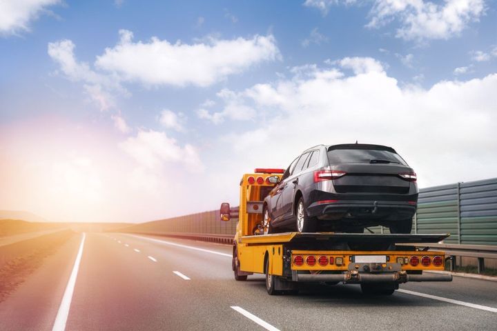 Black SUV loaded on a yellow tow truck driving on a highway at sunrise