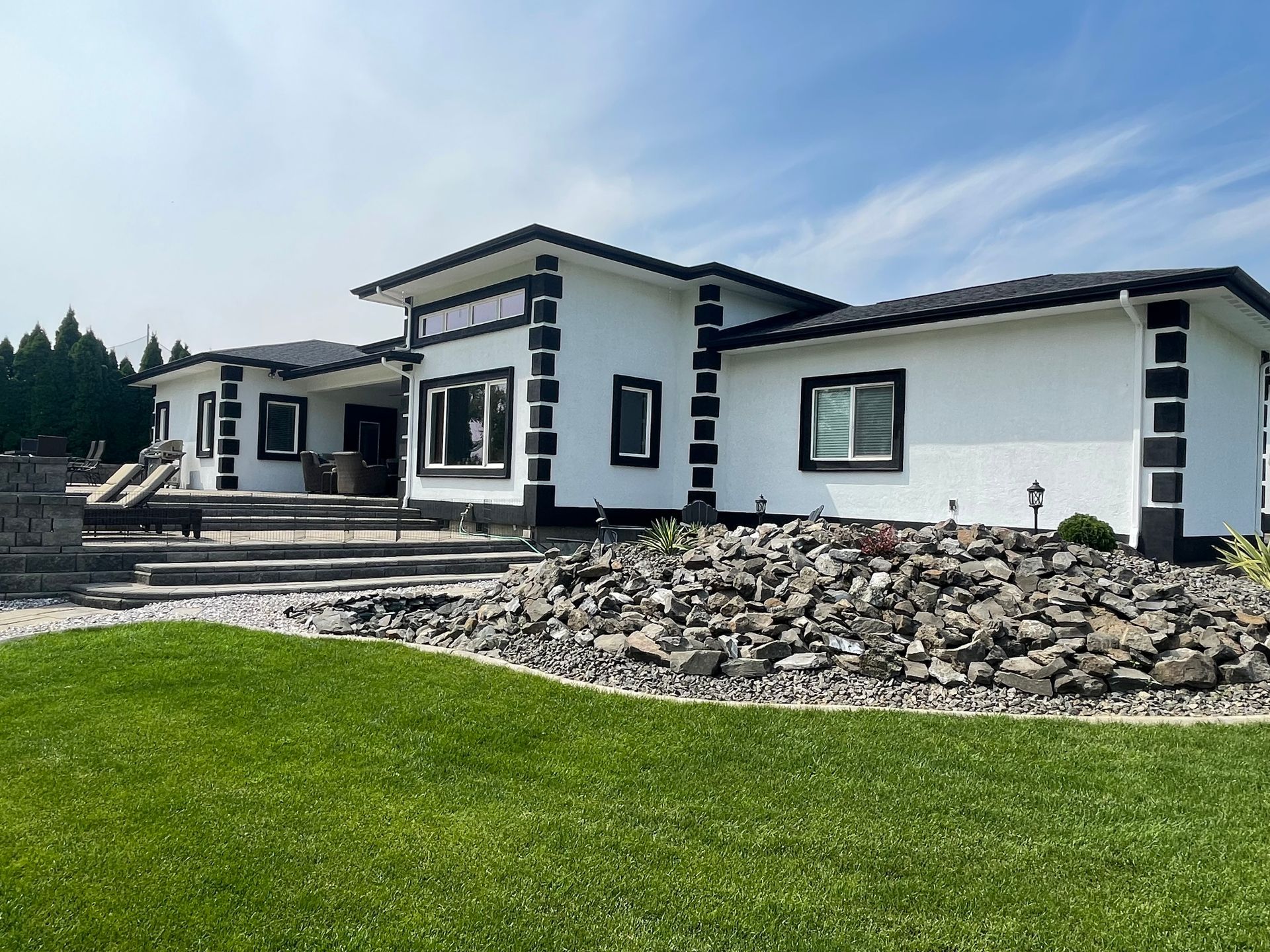 A large white house with black trim is sitting on top of a lush green lawn.