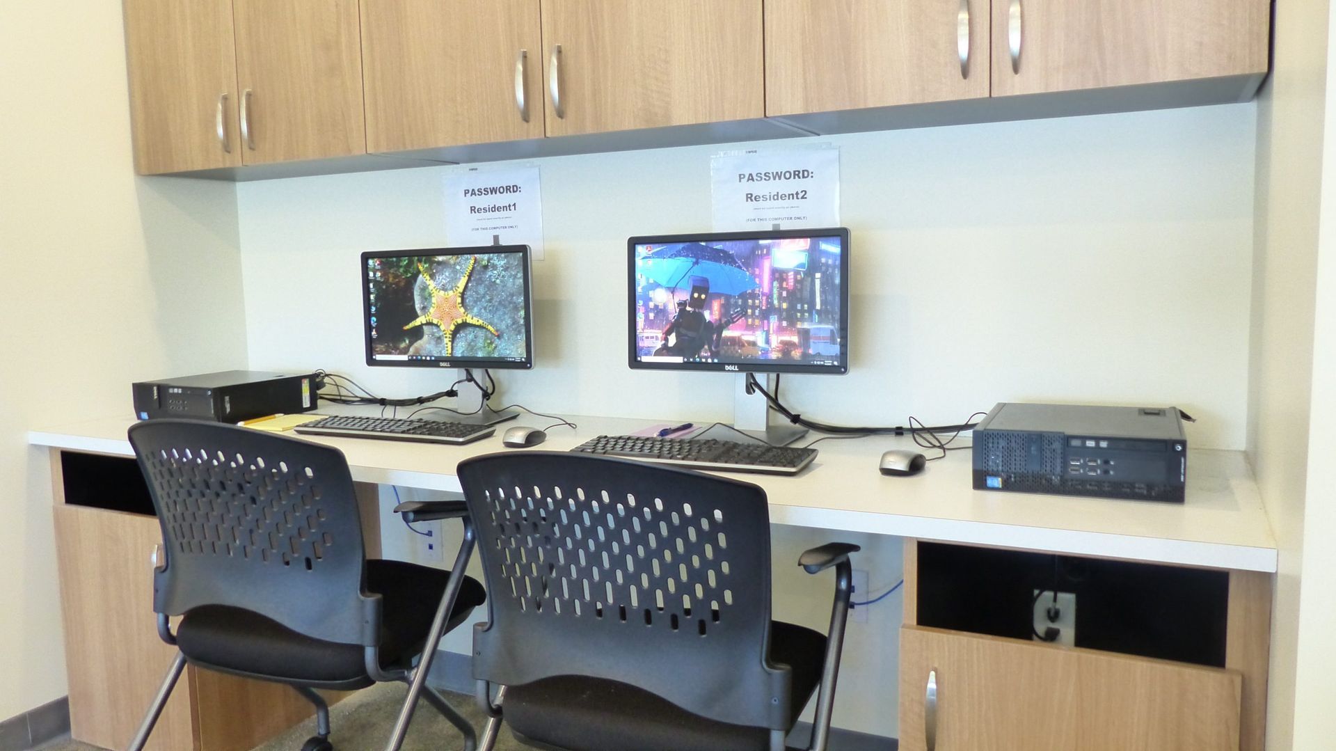 Office workstation with two monitors, two chairs, and cabinets above a desk