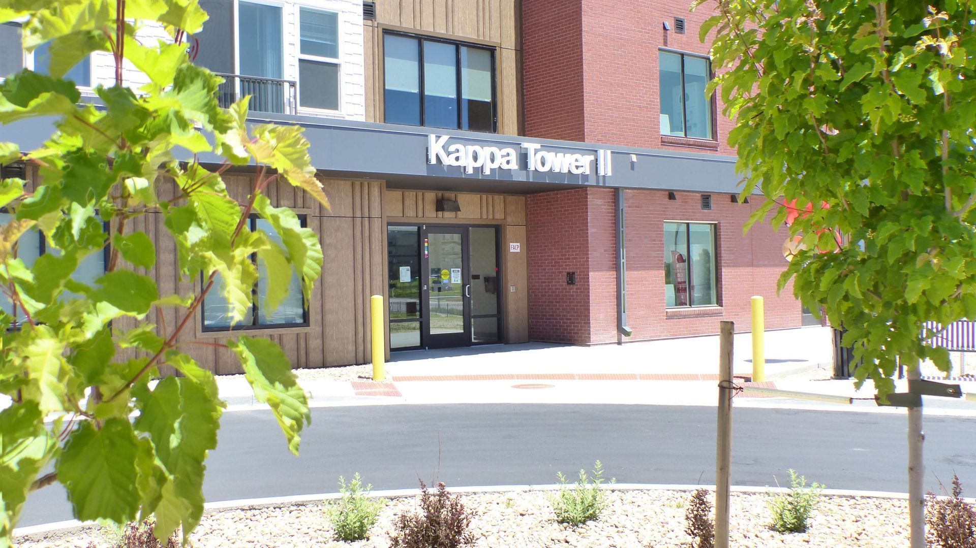 Entrance to Kappa Tower, a brick building with glass doors and leafy trees in front