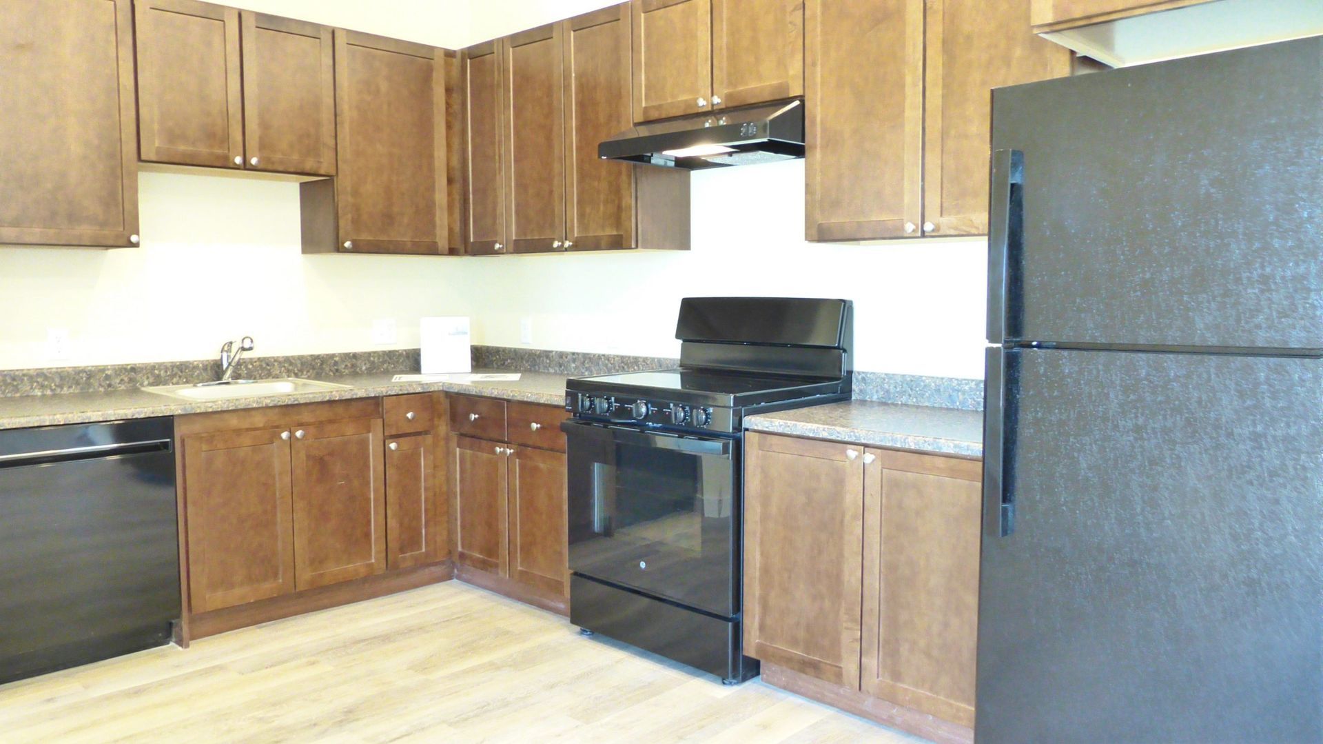 Empty kitchen with wood cabinets, black appliances, white countertops, and a light wood floor