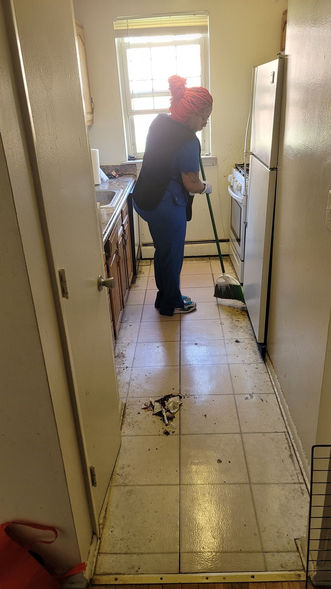 DAG personnel is standing in a kitchen cleaning the floor with a broom.