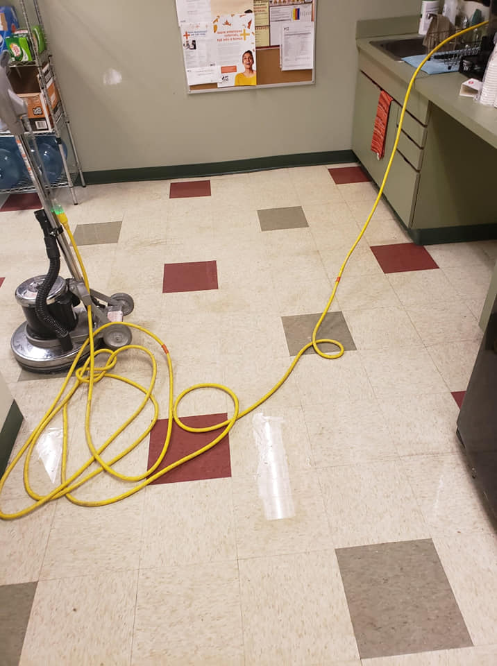 A vacuum cleaner is sitting on a tiled commercial floor in a kitchen.