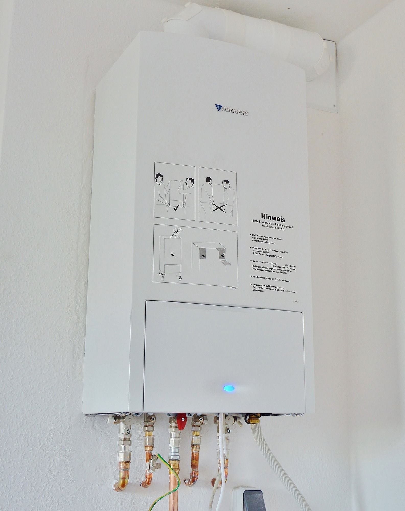 A white boiler is hanging on a white wall.