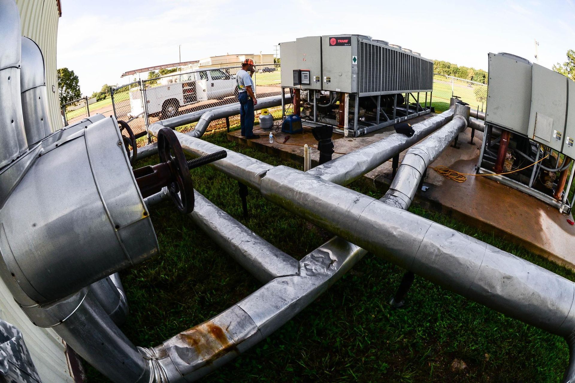 A man is working on a machine in a field surrounded by pipes.