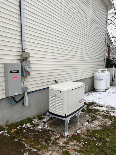 Outdoor backup generator beside a house, near electrical meters, on a snowy yard.