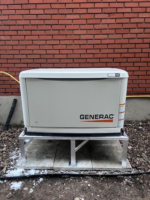 Gray Generac generator on a concrete pad against a red brick wall