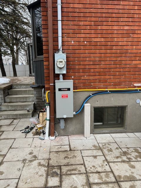 Electrical meter and gray utility box on a brick house exterior beside concrete steps and a basement window
