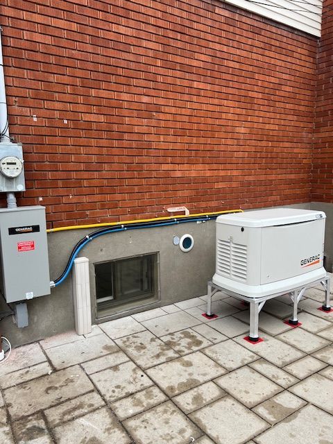 Outdoor utility area with brick wall, electrical box, vent, and white HVAC unit on tiled patio
