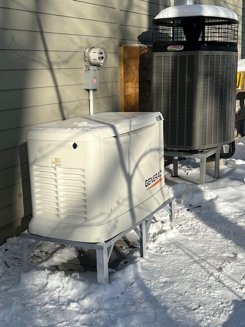 Two outdoor HVAC units beside a house, with snow on the ground and sunlight casting shadows.