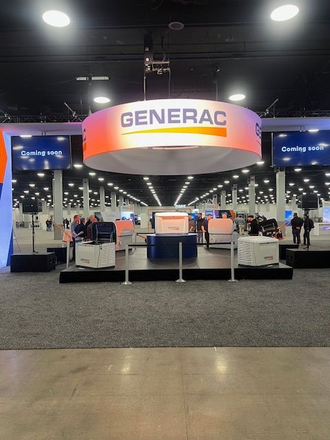 Generac trade show booth with large hanging sign and staff at display tables in an expo hall