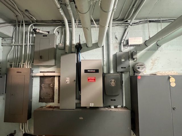 Industrial electrical panel room with gray cabinets, conduit, and wall-mounted equipment
