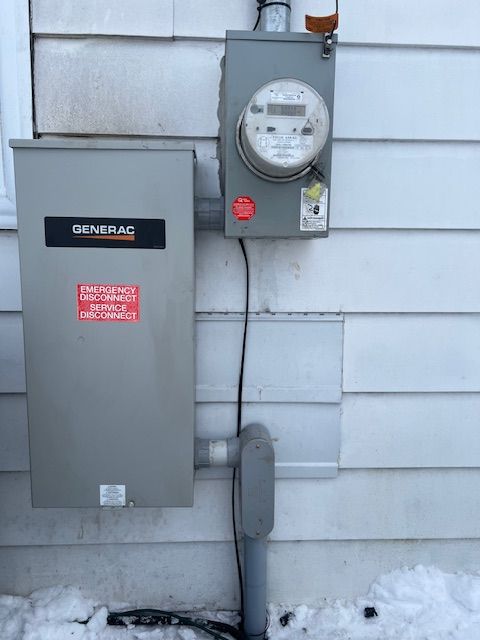 Gray electrical meter and breaker box mounted on an exterior house wall with conduit below.