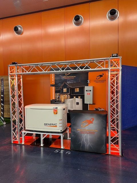 Industrial equipment displayed in a metal truss booth against an orange wall, with a machine and drums.