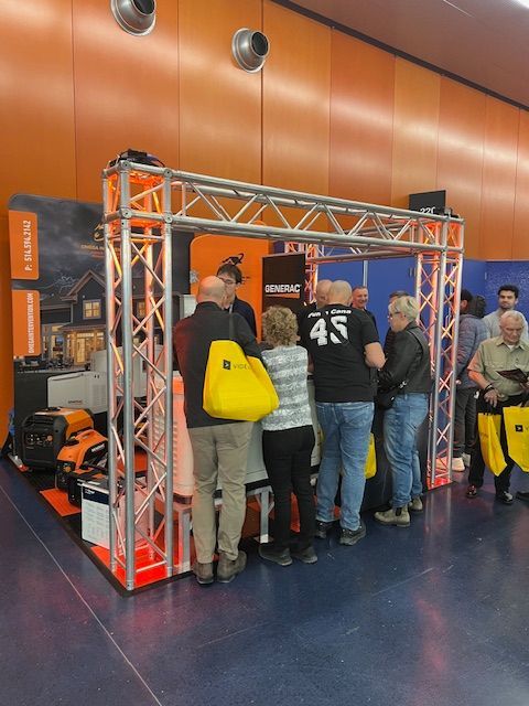 People gathered around a silver truss booth in a gymnasium, with orange walls and a yellow bag in front.