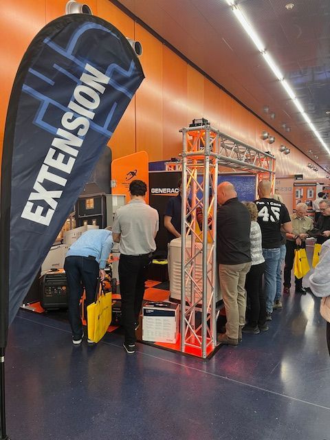 Trade show booth with an “EXTENSION” banner, orange display frame, and people browsing in a tunnel-like venue