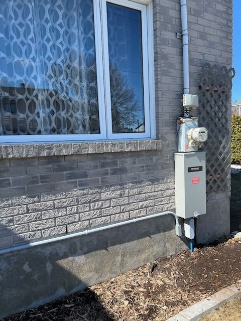 House exterior with a window and mounted utility meter panel beside a brick wall