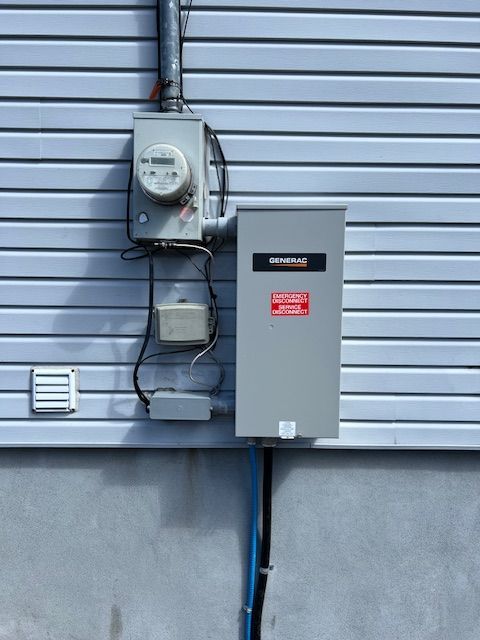 Electrical meters and gray utility boxes mounted on a corrugated exterior wall.