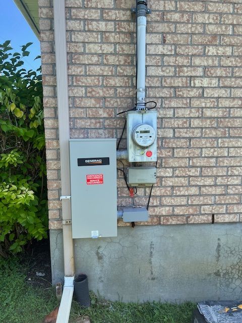 Utility meters and electrical boxes mounted on a brick house exterior near a downspout.