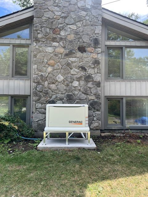 Stone house exterior with a white generator unit on a small concrete pad in the yard