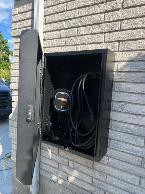 Outdoor EV charging station recessed into a gray brick wall, with charging cable coiled inside.