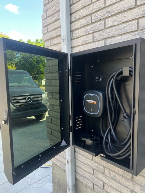 Open black outdoor EV charger cabinet mounted on a brick wall, with coiled cable and mirrored door.