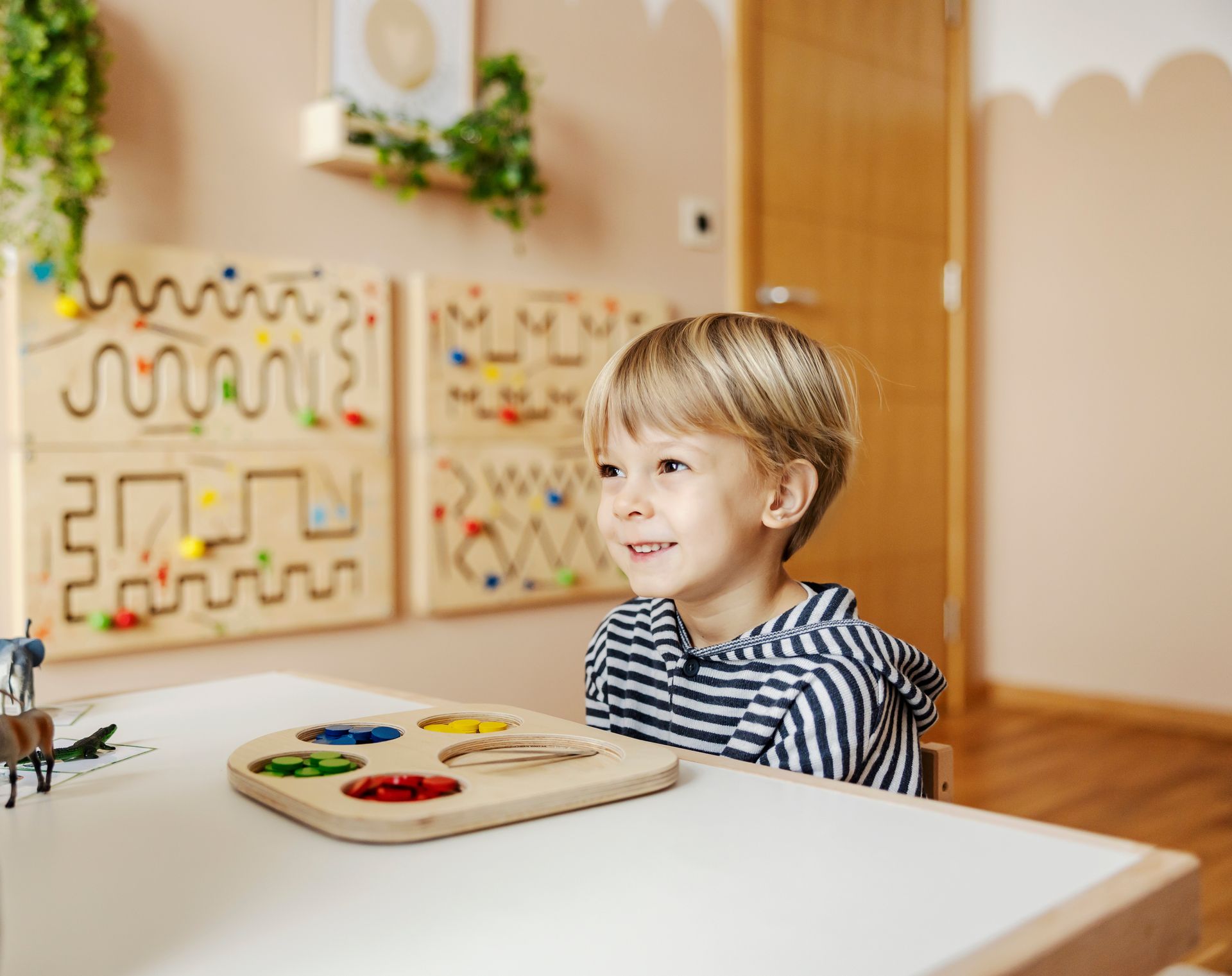 Young boy smiling at a table with a wooden Montessori color-sorting tray.