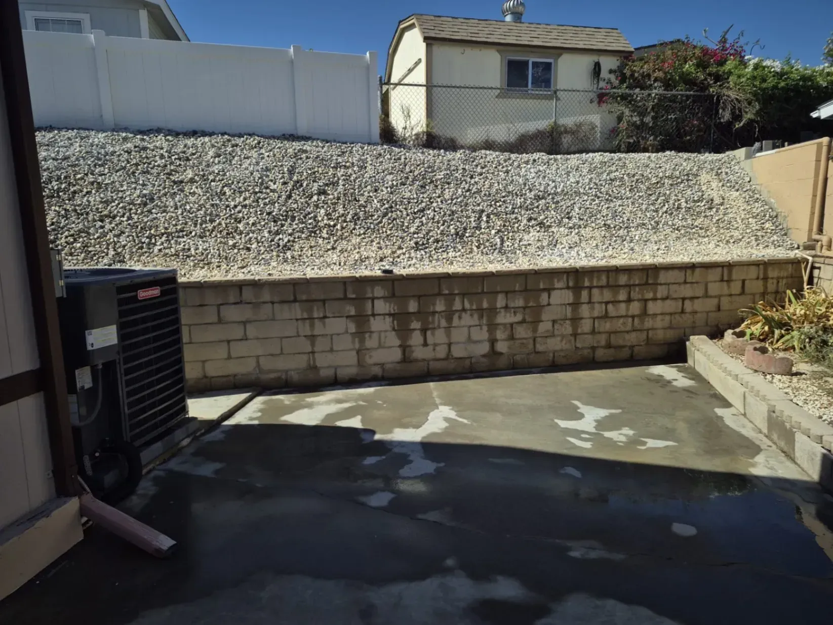 Backyard with a concrete patio, retaining wall, and rocky hillside. An air conditioning unit is in the foreground.