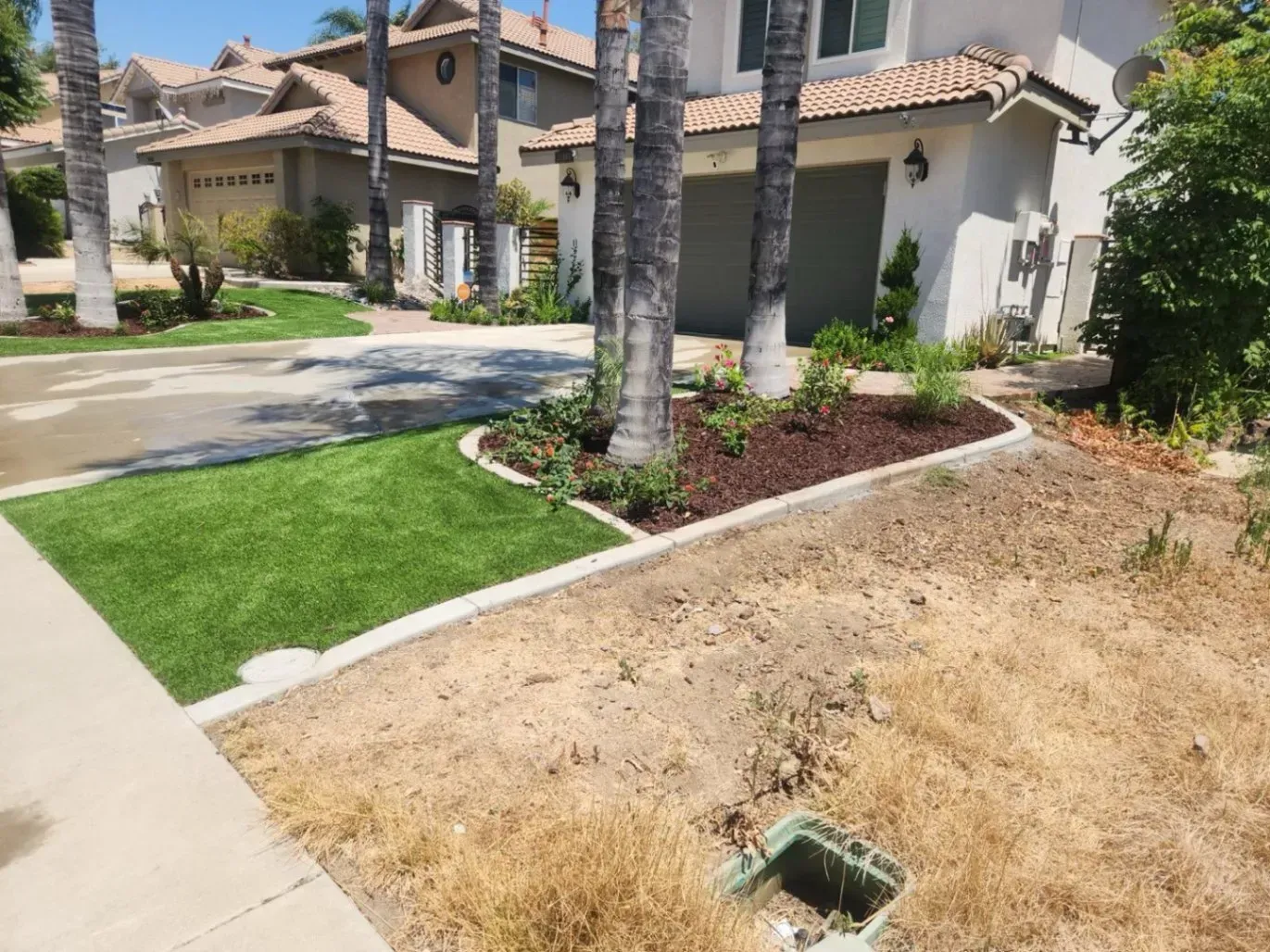 Residential front yard with artificial turf, brown mulch beds, and a driveway.