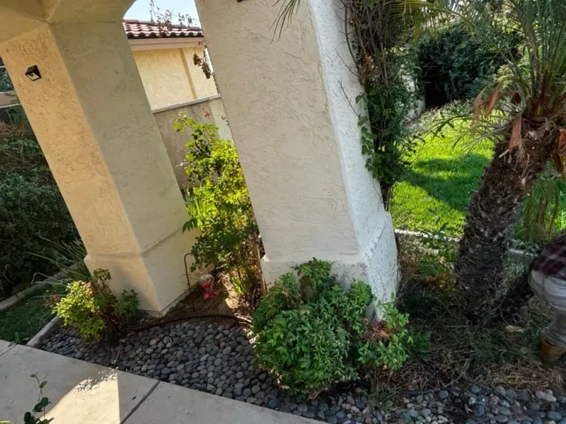 Beige pillars frame a garden with lush greenery and a lawn.