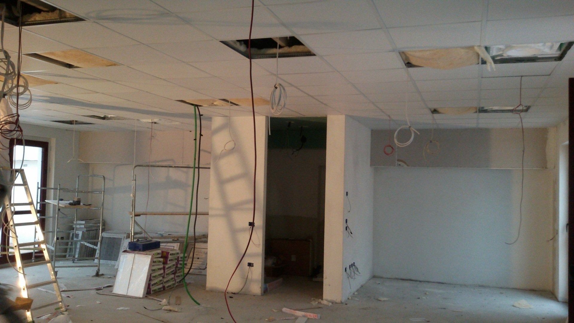 Stanza vuota in fase di ristrutturazione con controsoffitto a vista, scale e materiali edili.