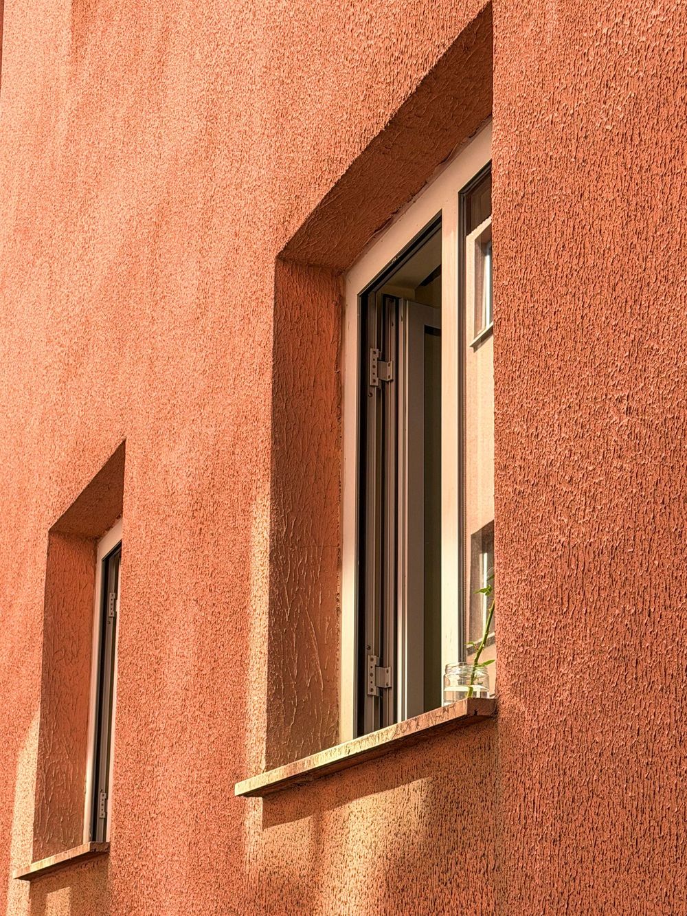 Facciata dell'edificio in stucco rosa con due finestre aperte e finiture bianche.